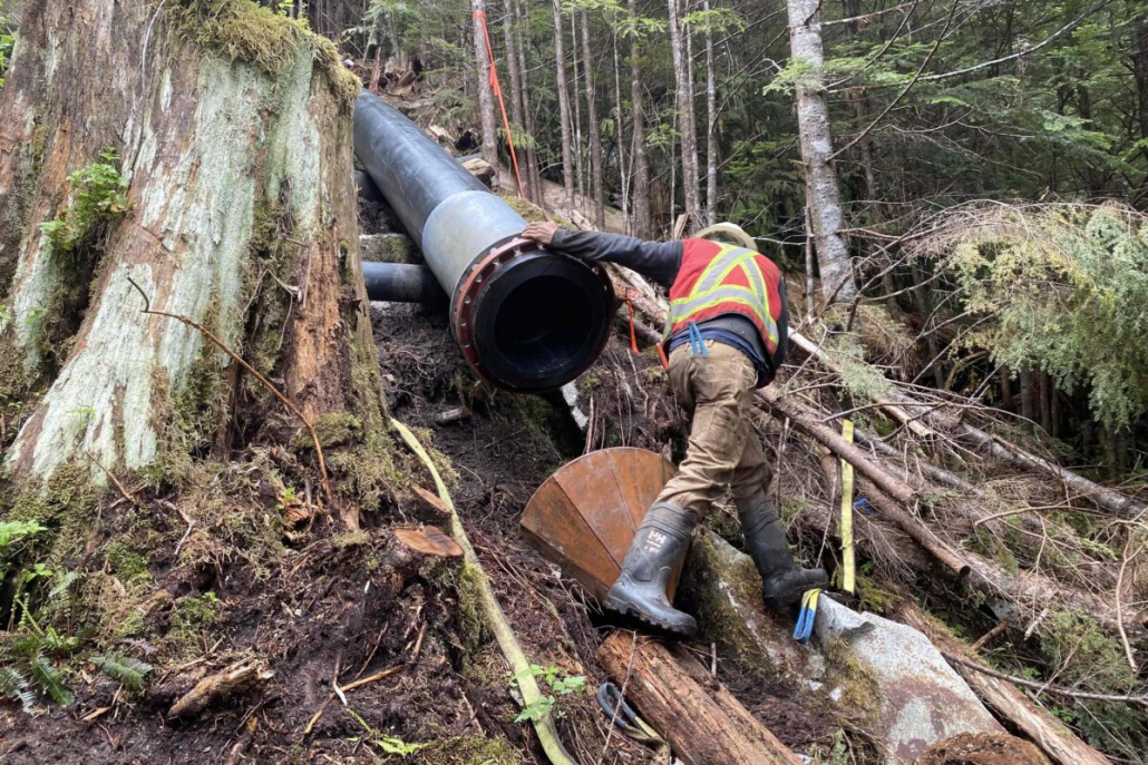 A man wearing a high-vis vest installs a pipe as part of a hydropower project in a forest.