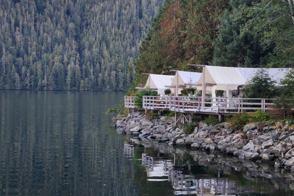Three lodges with canvass roofs sit at the edge of the forest looking out onto a very still Clayoquot Sound at Clayoquot Wilderness Lodge.