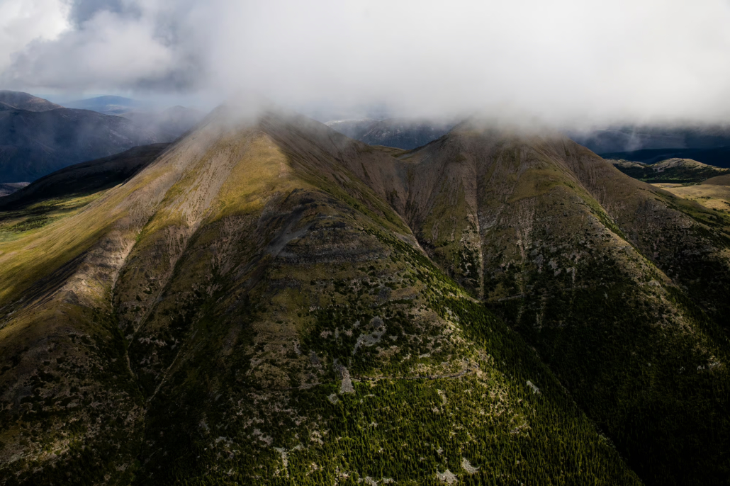 An aerial view of The Klinse-za (Twin Sisters) Mountains with grey, low hanging clouds hovering above them.