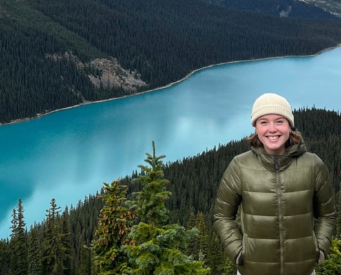 Issy stands on a mountain with Peyto Lake in the background behind her.