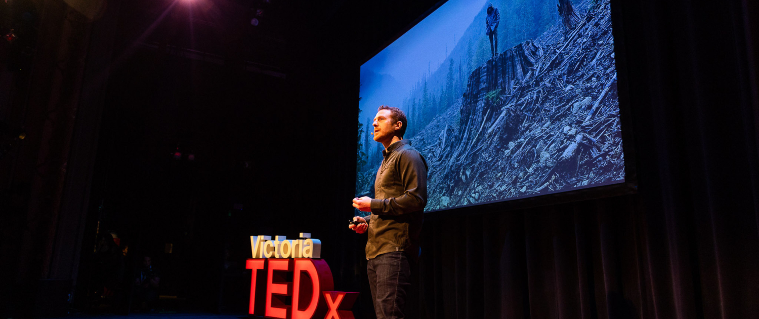 TJ stands on the TEDx stage with a photo of a foggy clearcut in the background.