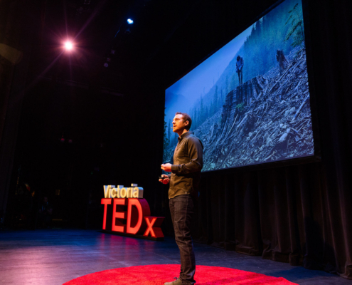 TJ stands on the TEDx stage with a photo of a foggy clearcut in the background.