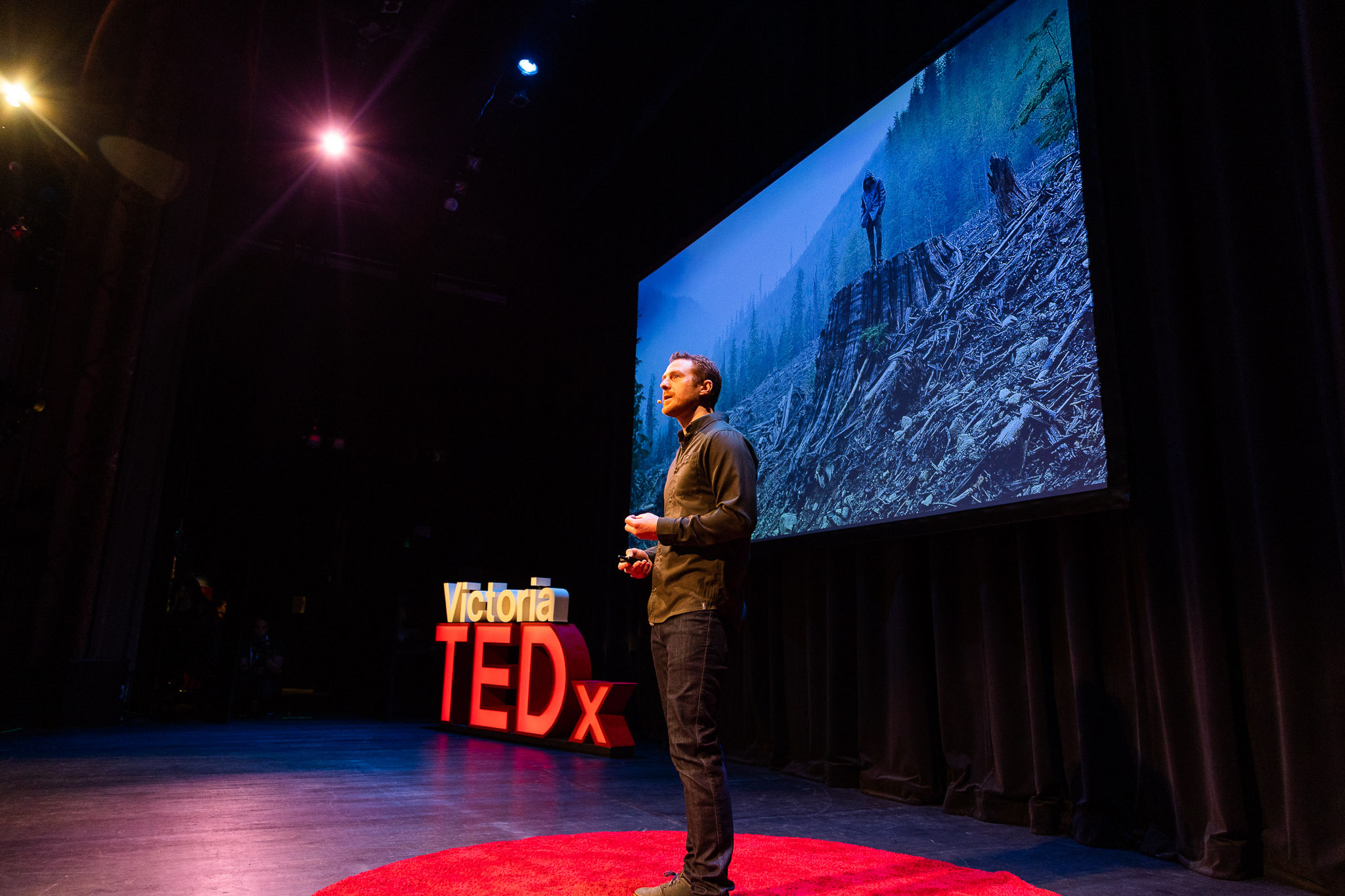 TJ stands on the TEDx stage with a photo of a foggy clearcut in the background.