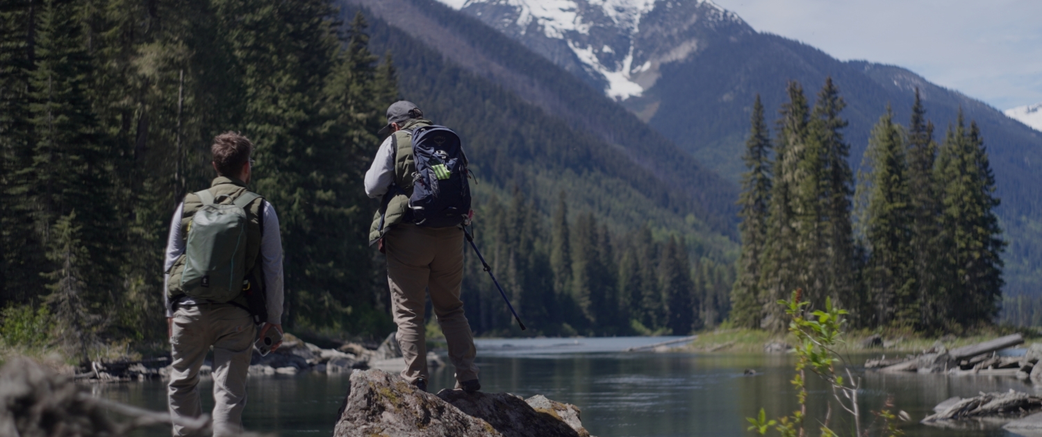 Two people stand on a rock by the Fraser River in Kanaka Bar territory.