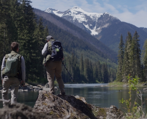 Two people stand on a rock by the Fraser River in Kanaka Bar territory.